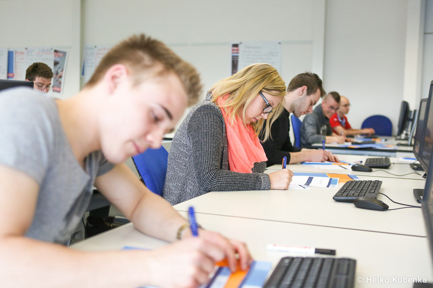 Teilnehmende eines Seminares schreiben auf Arbeitsblätter Auszubildende nehmen an einem Seminar teil und schreiben auf Arbeitsblätter, während sie vor Computern sitzen